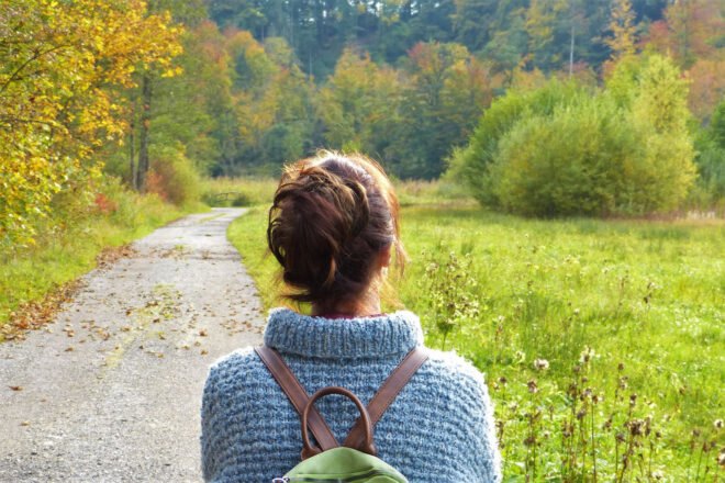 woman walking along a paved pathway surrounded by nature