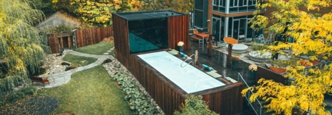 wooden box structure with large dark glass facade leading out to swimming pool