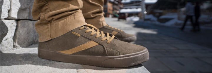 person wearing brown shoes standing on pavement with snow in the background