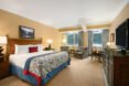 view of a suite with large bed and light brown colored carpet with large windows showing mountain views