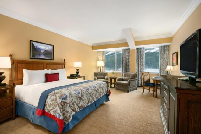 view of a suite with large bed and light brown colored carpet with large windows showing mountain views
