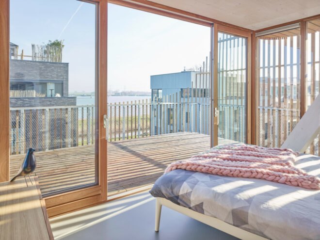 gray bed facing glass walls open to a wood balcony
