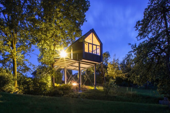 black gabled treehouse lit from within at night