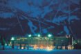 hotel with mountains in the background surrounded by trees and snow at night