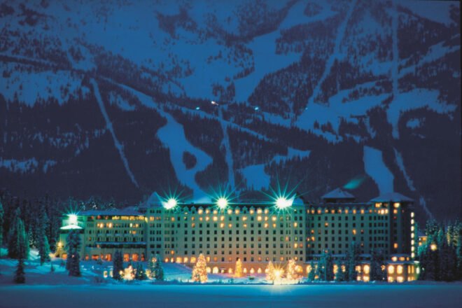 hotel with mountains in the background surrounded by trees and snow at night