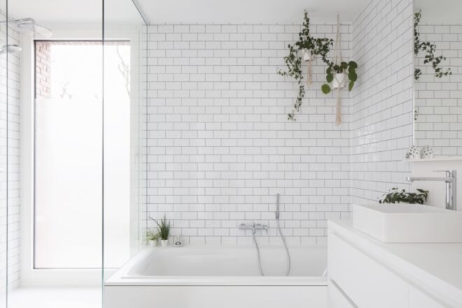 white tiles and walls adorn the bathroom with plants placed near tub
