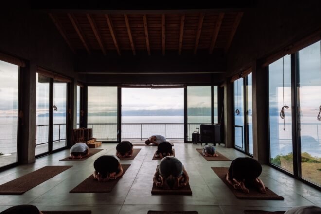 people doing yoga in room with glass walls overlooking the sea