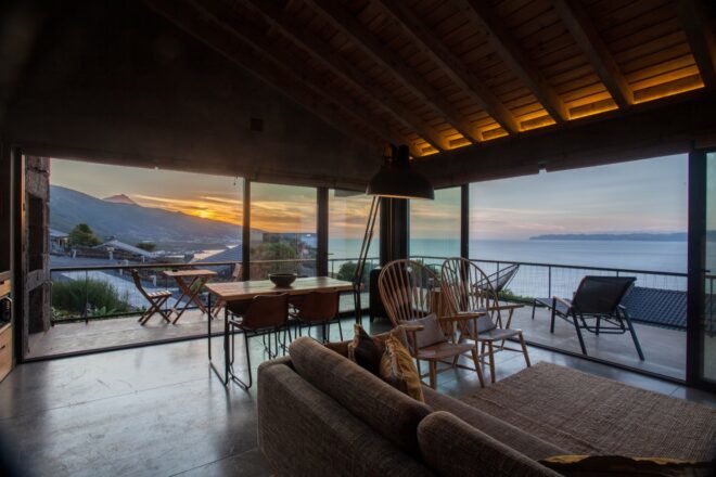 living room with gray sofa in room with glass walls at sunset