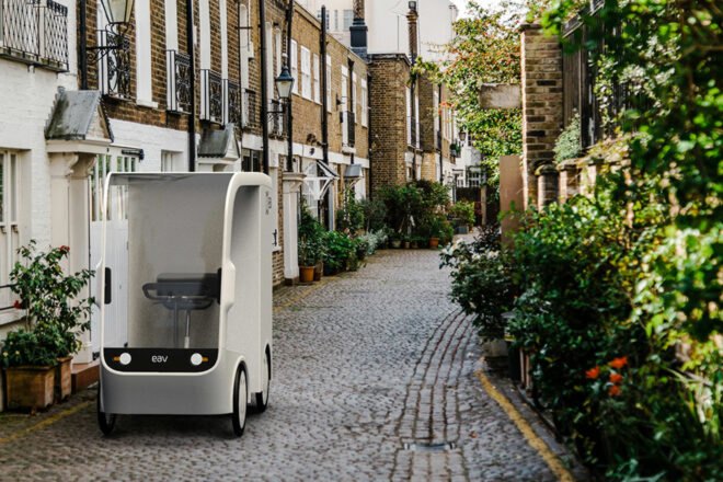 small white electric cargo quadricycle parked in the middle of a cobblestone street near homes
