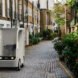 small white electric cargo quadricycle parked in the middle of a cobblestone street near homes