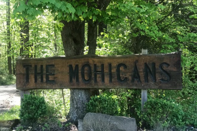wood sign that says The Mohicans in front of a tree surrounded by greenery