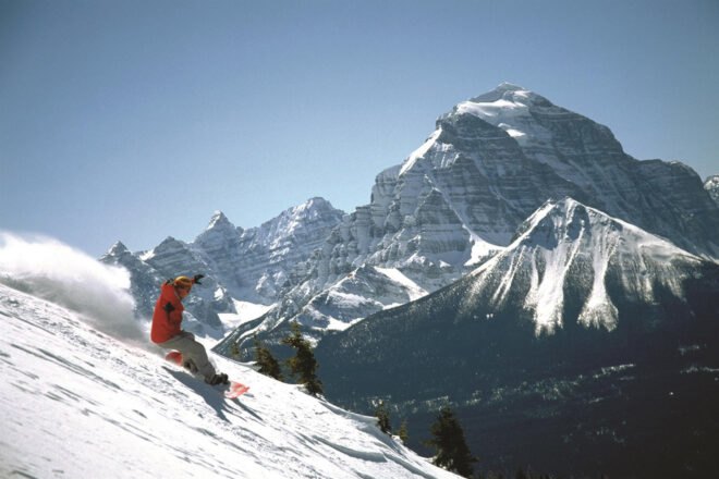 person snowboarding in daytime with snow covered mountains in the background