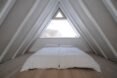 white bed in front of glass window under sloping ceilings