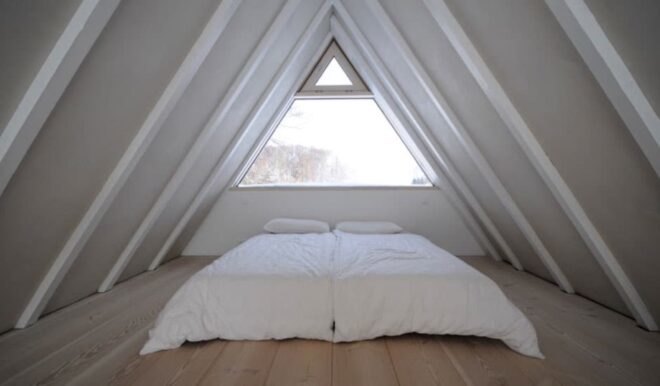 white bed in front of glass window under sloping ceilings