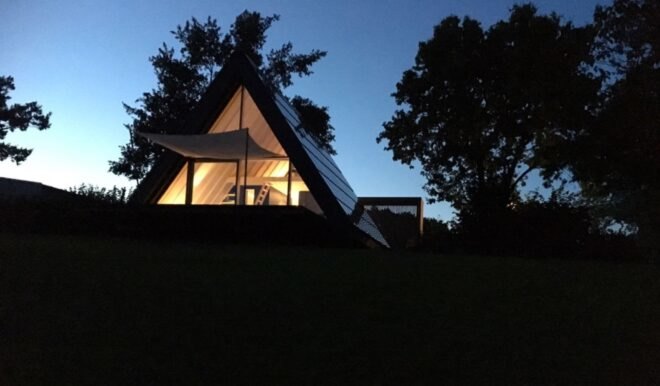 A-frame house with glass wall lit from within at night