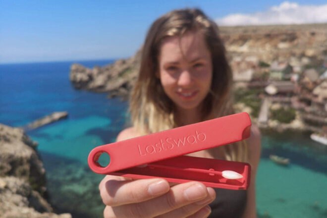woman on a beach holding a red reusable swab