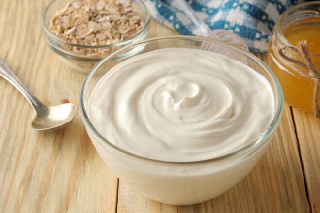 yogurt in a glass container with bowl of oatmeal and honey near by