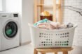 white plastic laundry basket filled with clothes placed on wooden stool in front of washing machine
