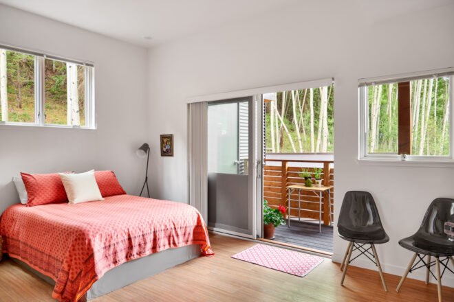 bedroom with red bed and a desk as well as a sliding door open to a wood balcony
