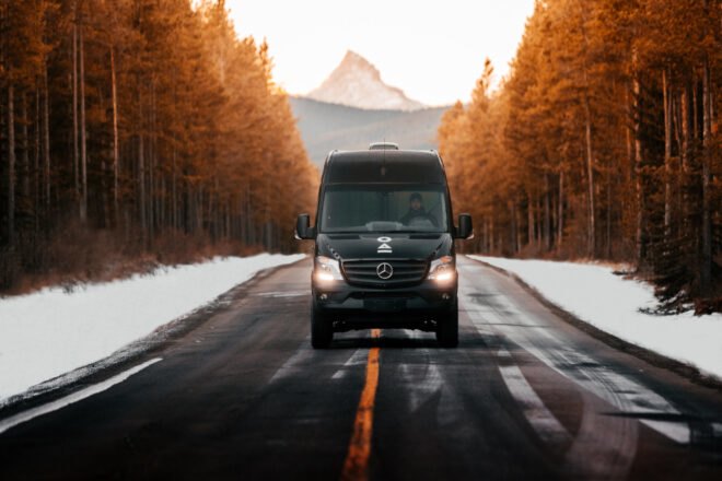 black van driving on road surrounded by snow