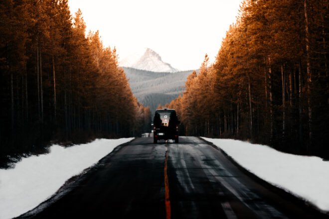 black van driving on road surrounded by snow