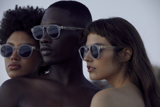 three models wear just humans sunglasses while near the ocean