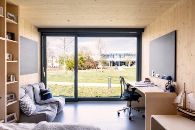 couches and a wooden desk are next to a large floor to ceiling window