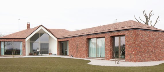 brick house with large ceiling to floor windows surrounded by grass