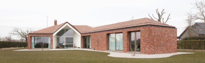 brick house with large ceiling to floor windows surrounded by grass