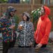 three friends in bright and patterned rain jackets drinking beer in the rain