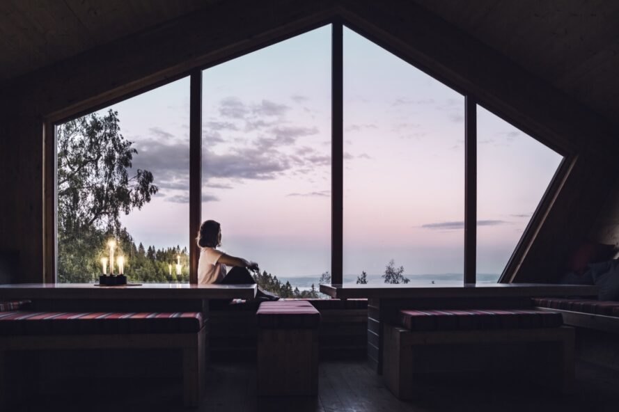 person sitting on bench near large window overlooking fjords at sunset
