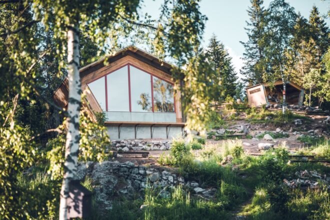 geometric wood cabin at top of tree-covered hillside