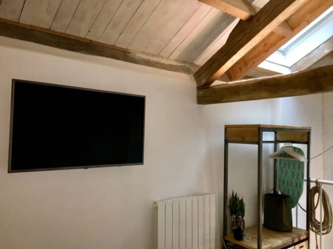 bedroom with wooden beams exposed in the ceiling and flat-screen TV on wall