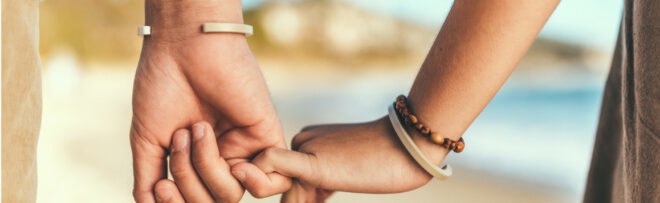 two people hold hands by the beach wearing bracelets made from recycled plastic