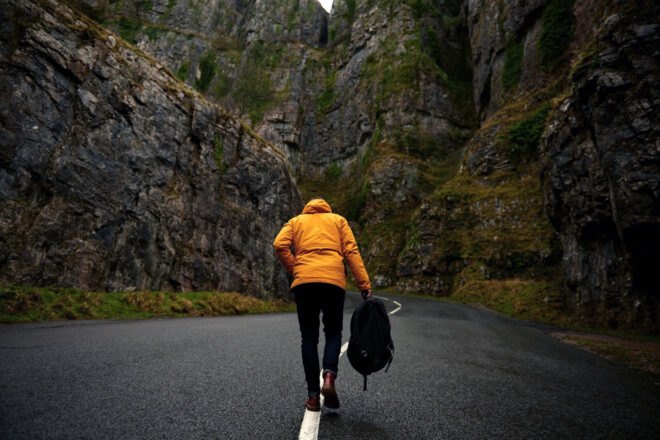 person in yellow jacket walking on road near mountains
