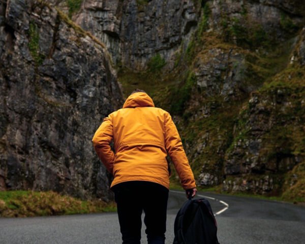 person in yellow jacket walking on road near mountains