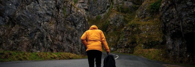 person in yellow jacket walking on road near mountains