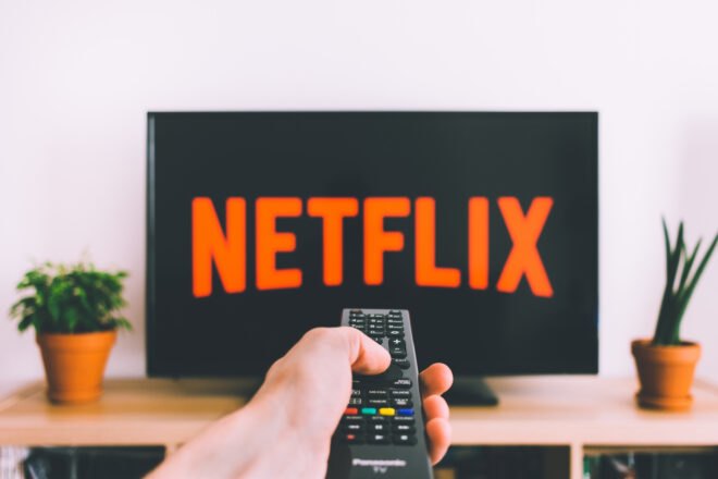 Person using remote to turn on Netflix on TV