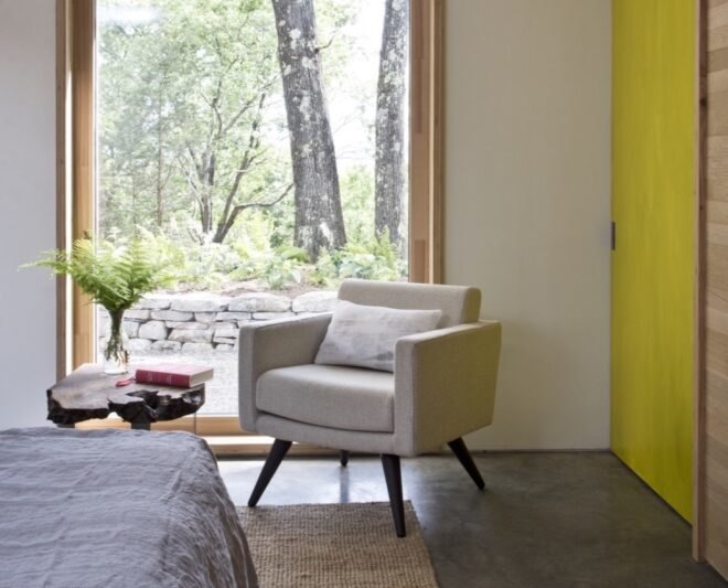 small beige chair by a bed and a large window