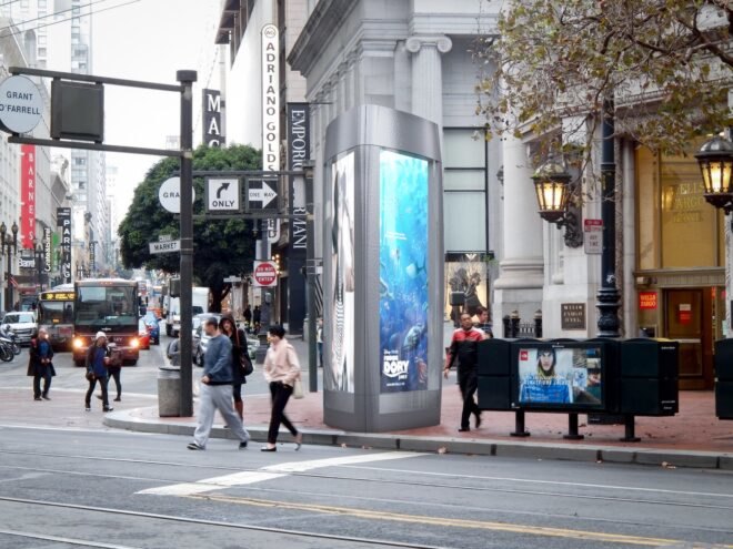 small curved metal bathroom unit with digital advertisements on the side in a city