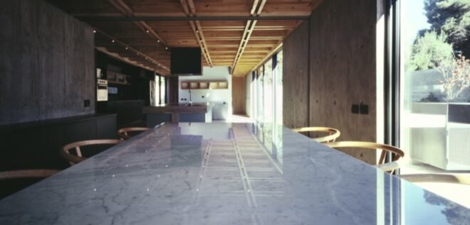 white dining table in foreground with kitchen with wood cabinetry in background