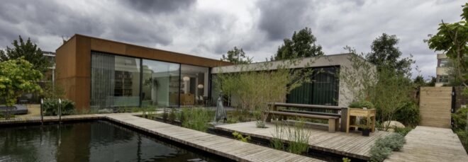 home with weathered steel exterior and wood walkway over a natural pool