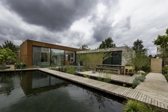 home with weathered steel exterior and wood walkway over a natural pool