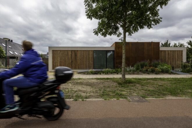 motorcycle driving past home with weathered steel exterior