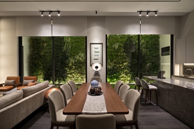 wood dining table in front of tall windows with views of a green wall