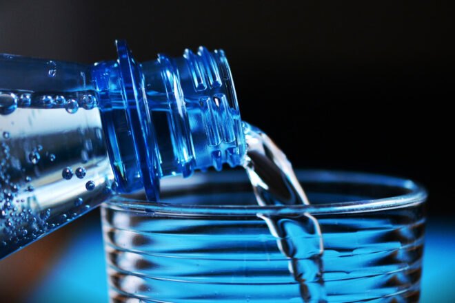 water from plastic bottle being poured into glass cup