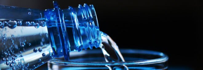 water from plastic bottle being poured into glass cup