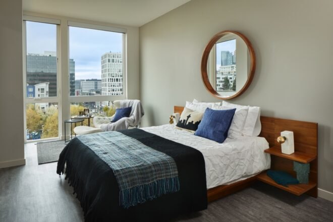 bedroom with blue and white bed and tall windows revealing views of Seattle