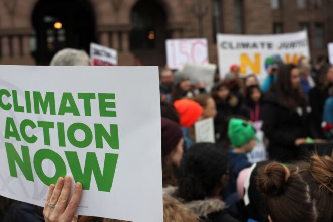 people of all ages striking with one person holding sign that reads "Climate Action Now"