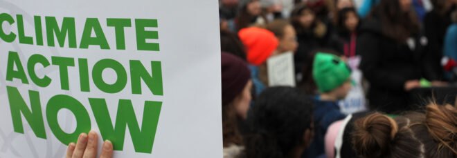 people of all ages striking with one person holding sign that reads "Climate Action Now"